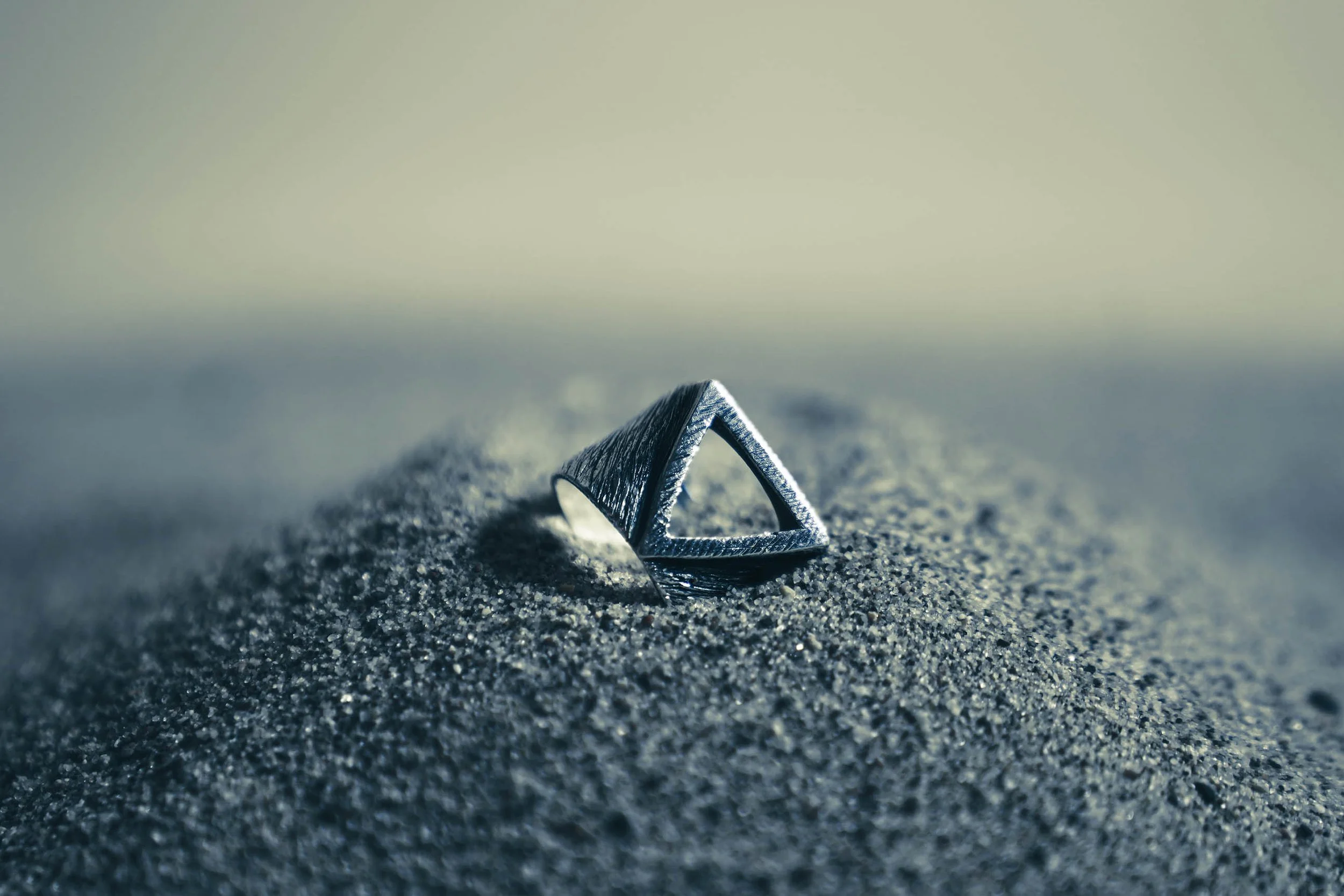 Artistic close-up of a geometric silver ring on a dark, textured surface