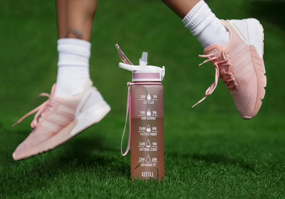 Dynamic fitness campaign detail of pink sneakers in motion beside a sports bottle on vivid green grass, captured with precise timing, clean product separation and selective focus that turns an everyday workout moment into advertising imagery