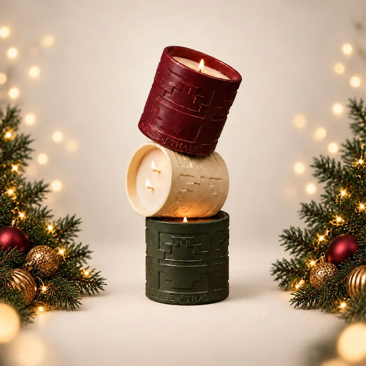Luxury Christmas candle campaign photography featuring stacked red, ivory and green candles framed by evergreen branches, ornaments and warm festive lights.