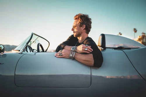 Man in sunglasses leaning on a classic Porsche convertible wearing Buck Palmer silver rings, bracelets and a watch