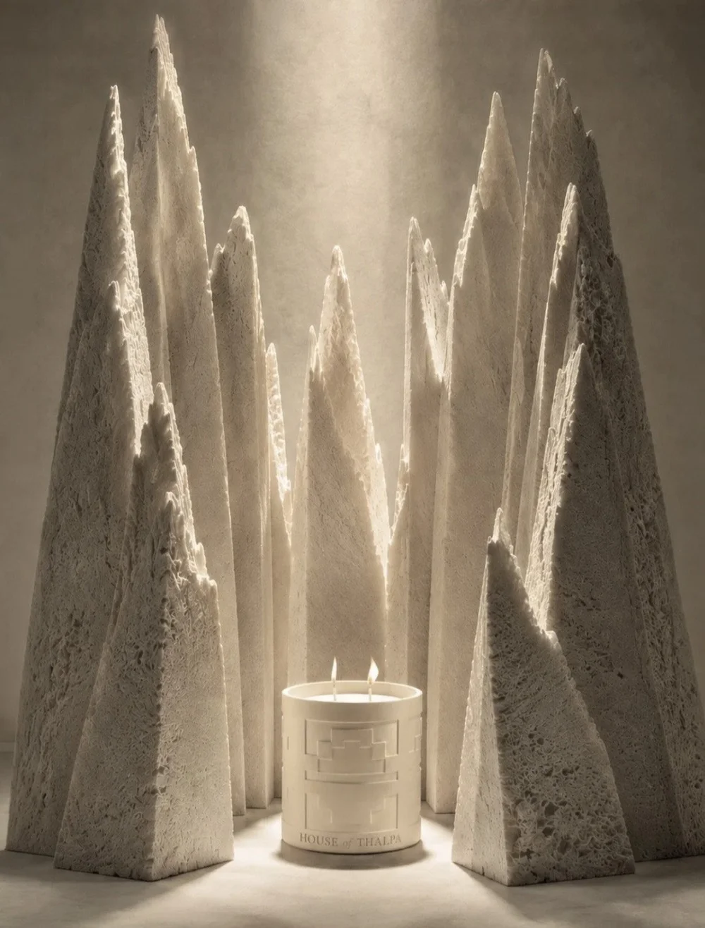 Luxury candle glowing among sculptural stone forms in warm, dramatic light