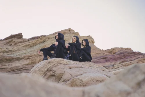 Three models in black Women of the Galaxy hoodies seated on a boulder at Vasquez Rocks, fall apparel campaign photography