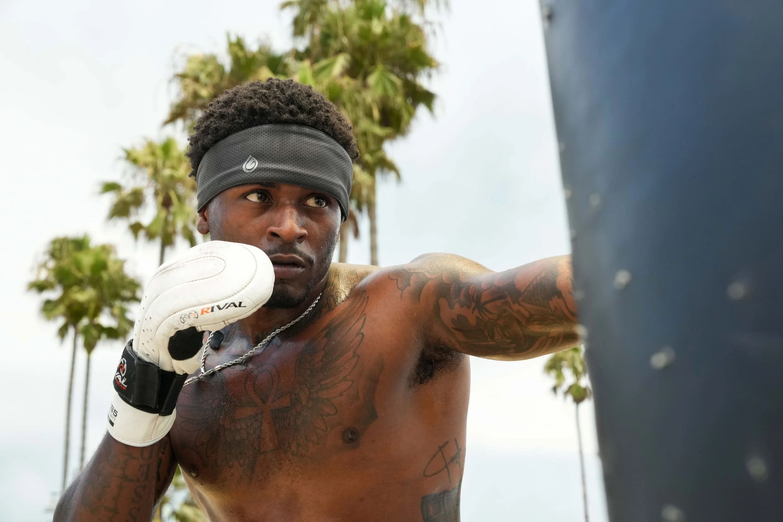 Boxer throwing a punch outdoors in white gloves and a Gymwrap performance headband, framed by palm trees and bright coastal daylight.
