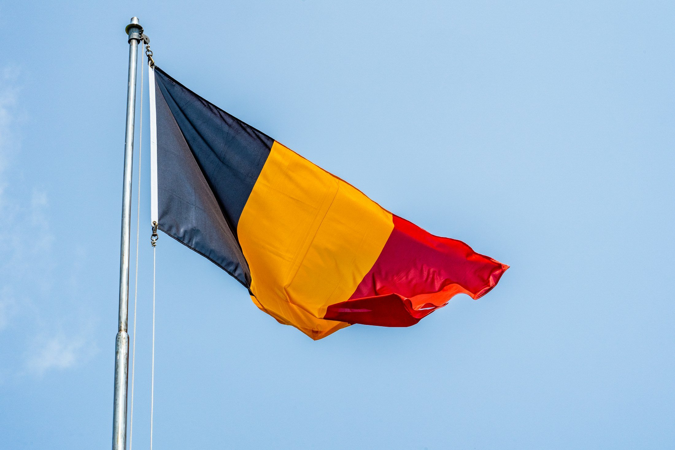 Le drapeau belge noir, jaune et rouge flotte au vent sur un mât, sous un ciel bleu