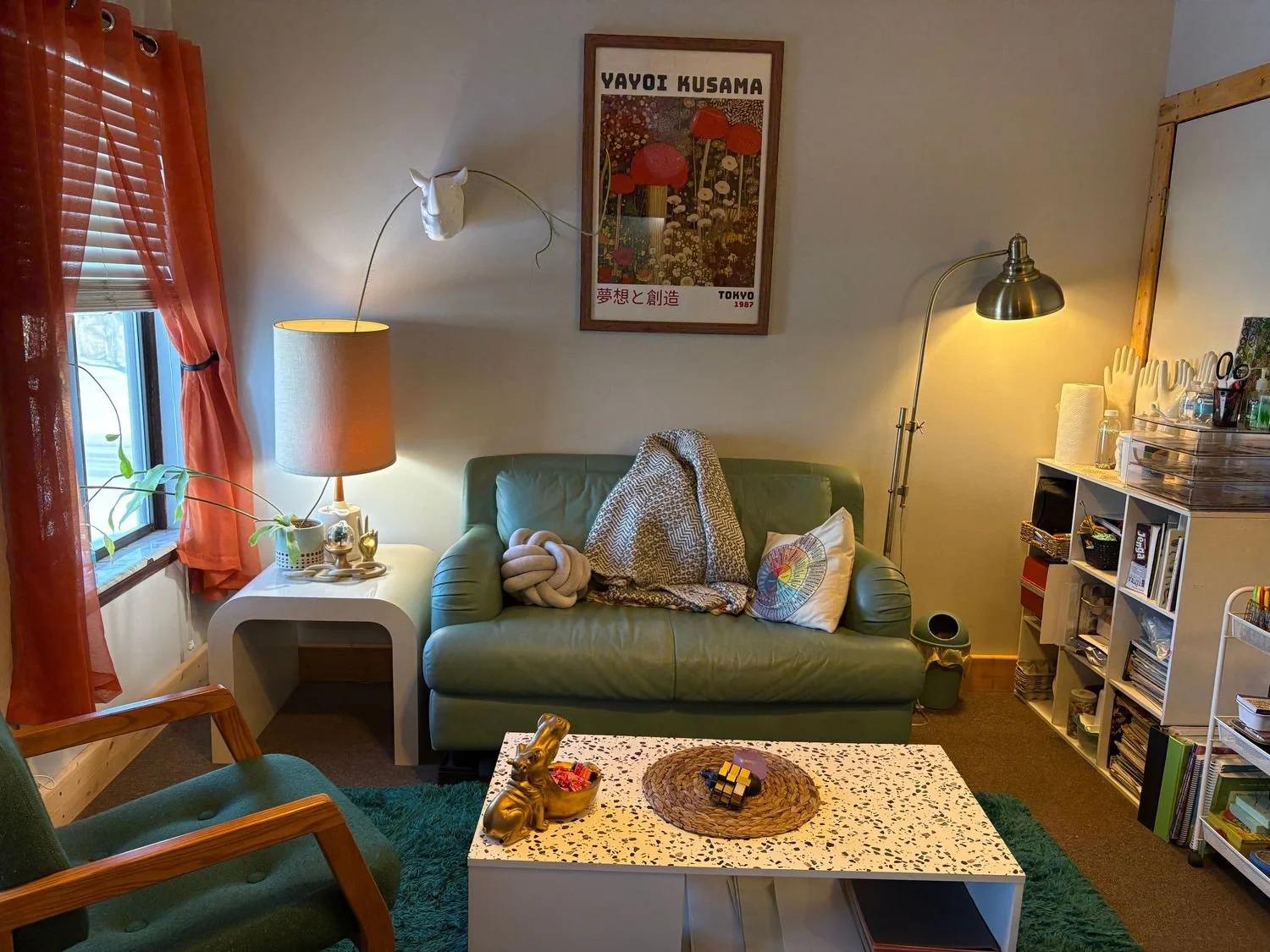 Jane’s office with a green loveseat, warm lighting, plants and colorful artwork