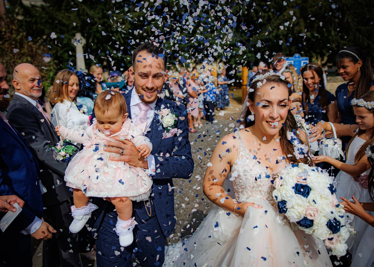 Bride and groom walking through confetti with their daughter at an Oxfordshire wedding