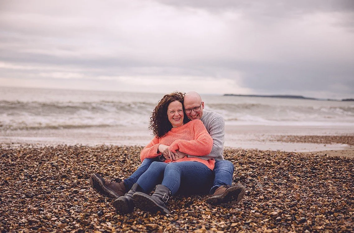 Engagement shoot: couple laughing together on a pebble beach