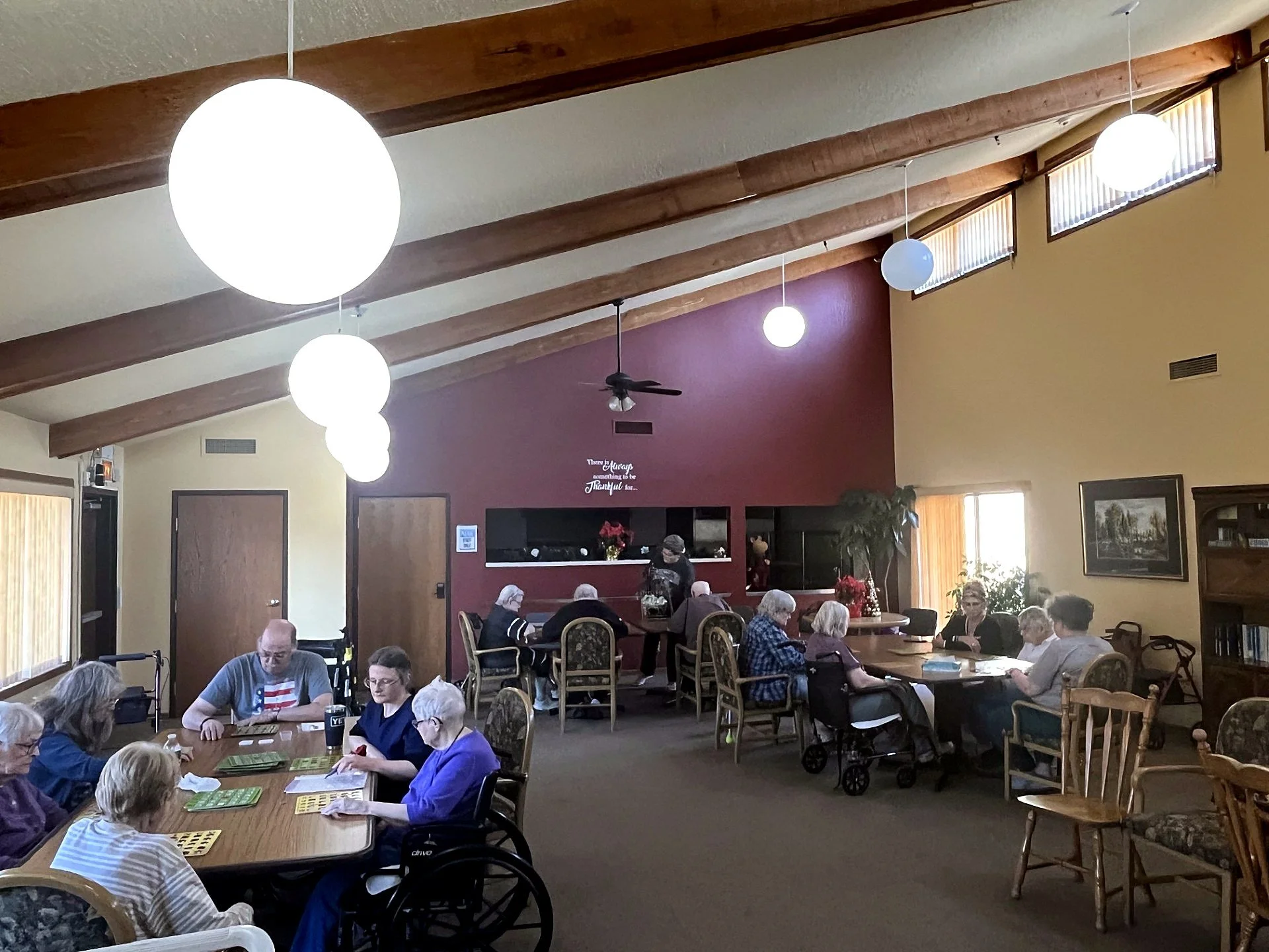 Residents playing bingo together in the community room, with a staff member helping out