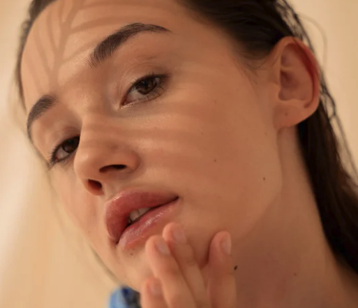 Woman gently touching her cheek, illustrating facial skincare at Recoupia in Lynnwood