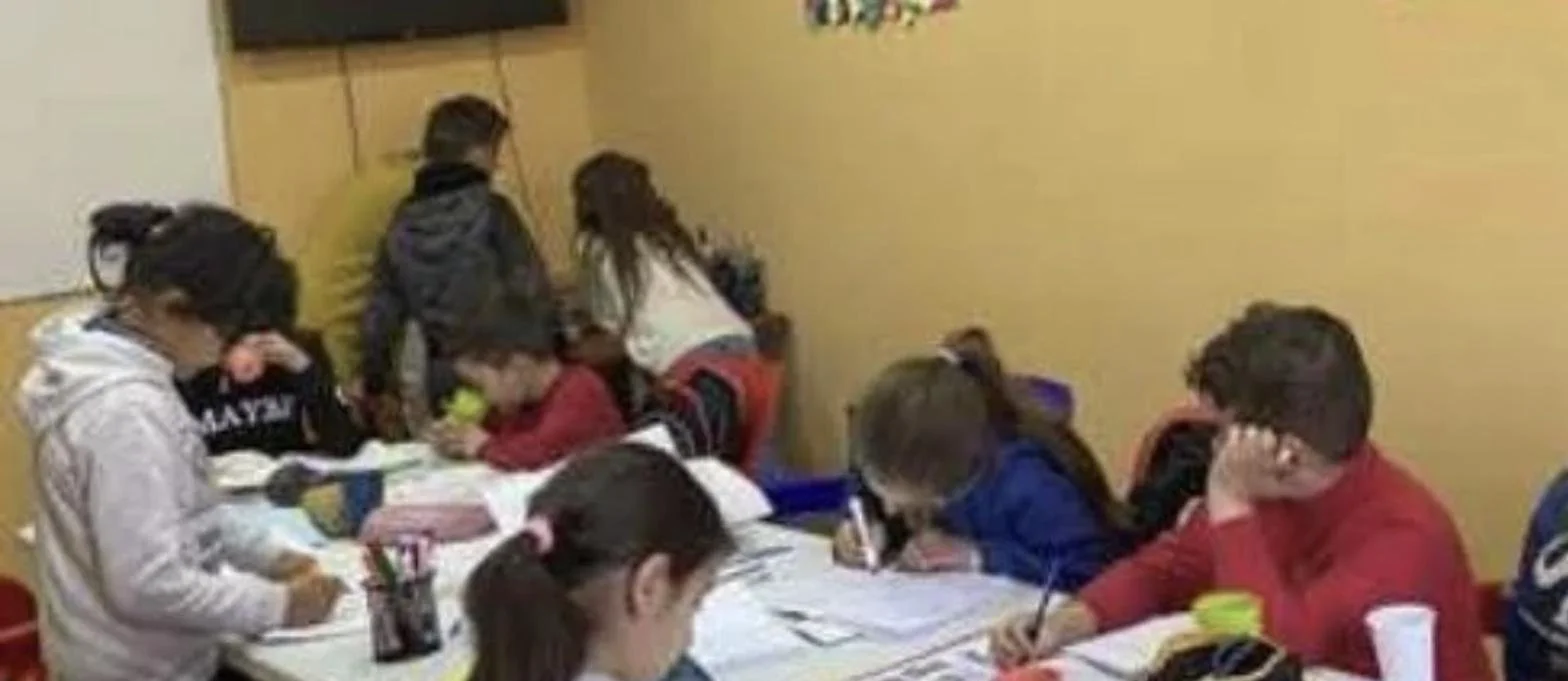 Children writing together in exercise books at a Tek Ura homework club table
