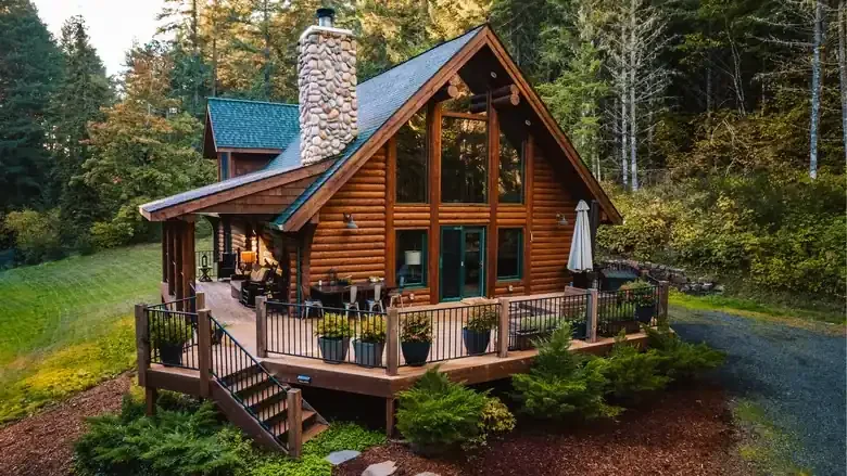 The cabin's wraparound deck with seating, beneath tall evergreens