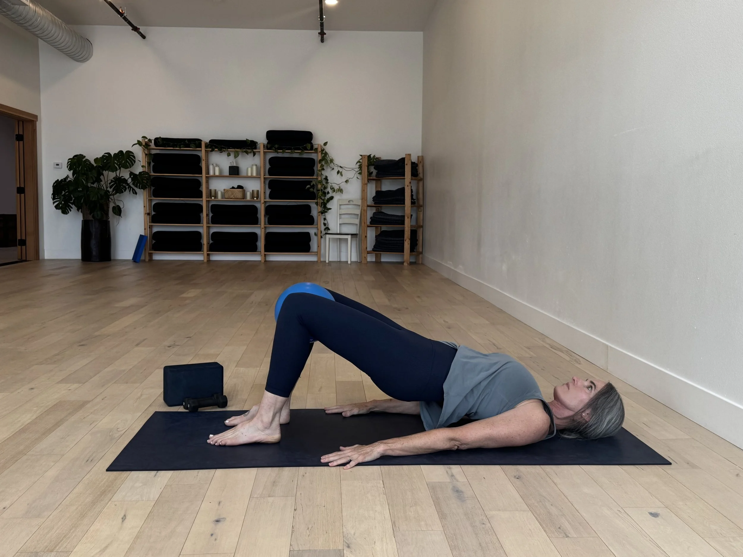 A student holding a bridge with a small ball between her knees in a classical pilates class