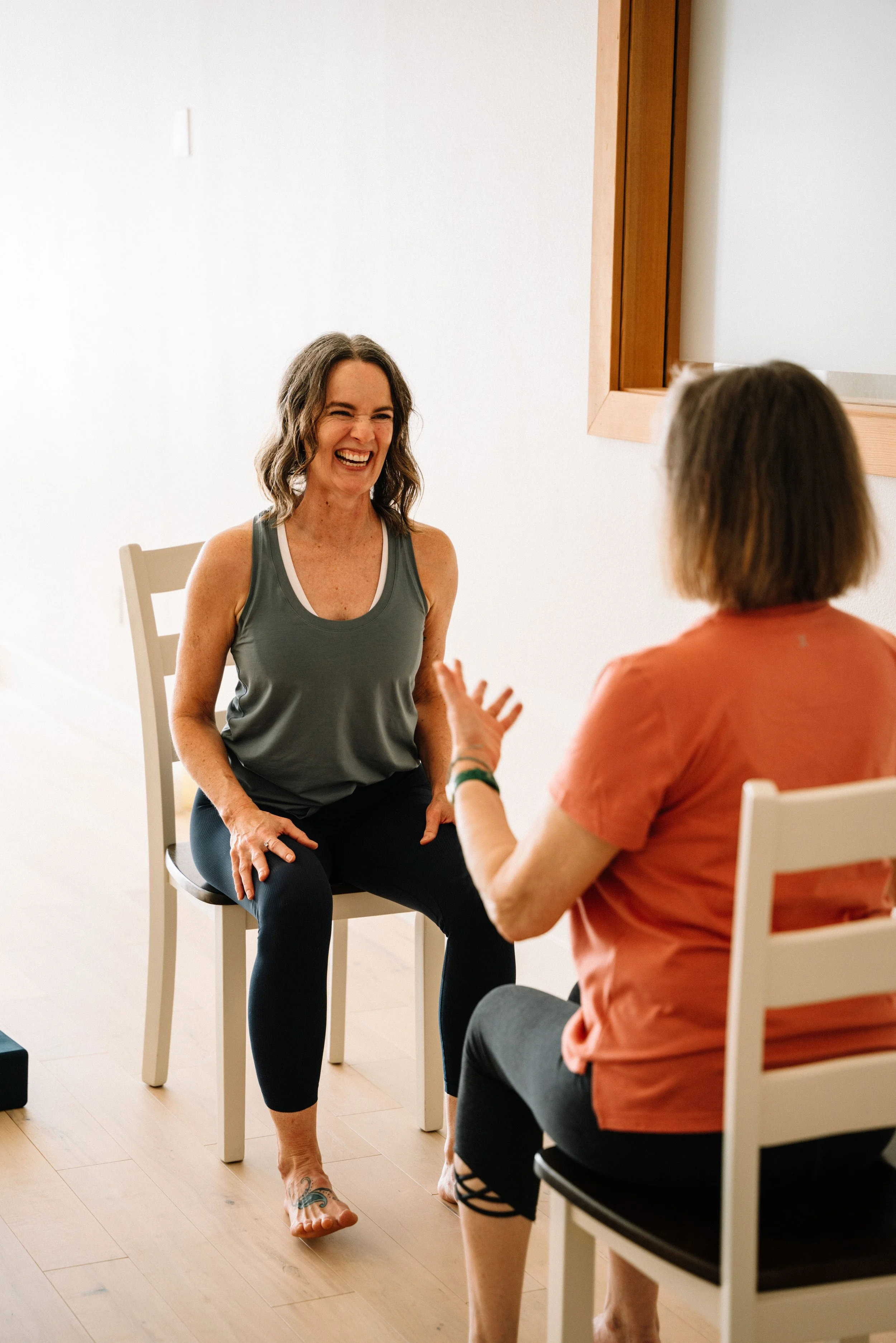 Two students laughing together in a chair yoga class at Lynden Yoga Collective