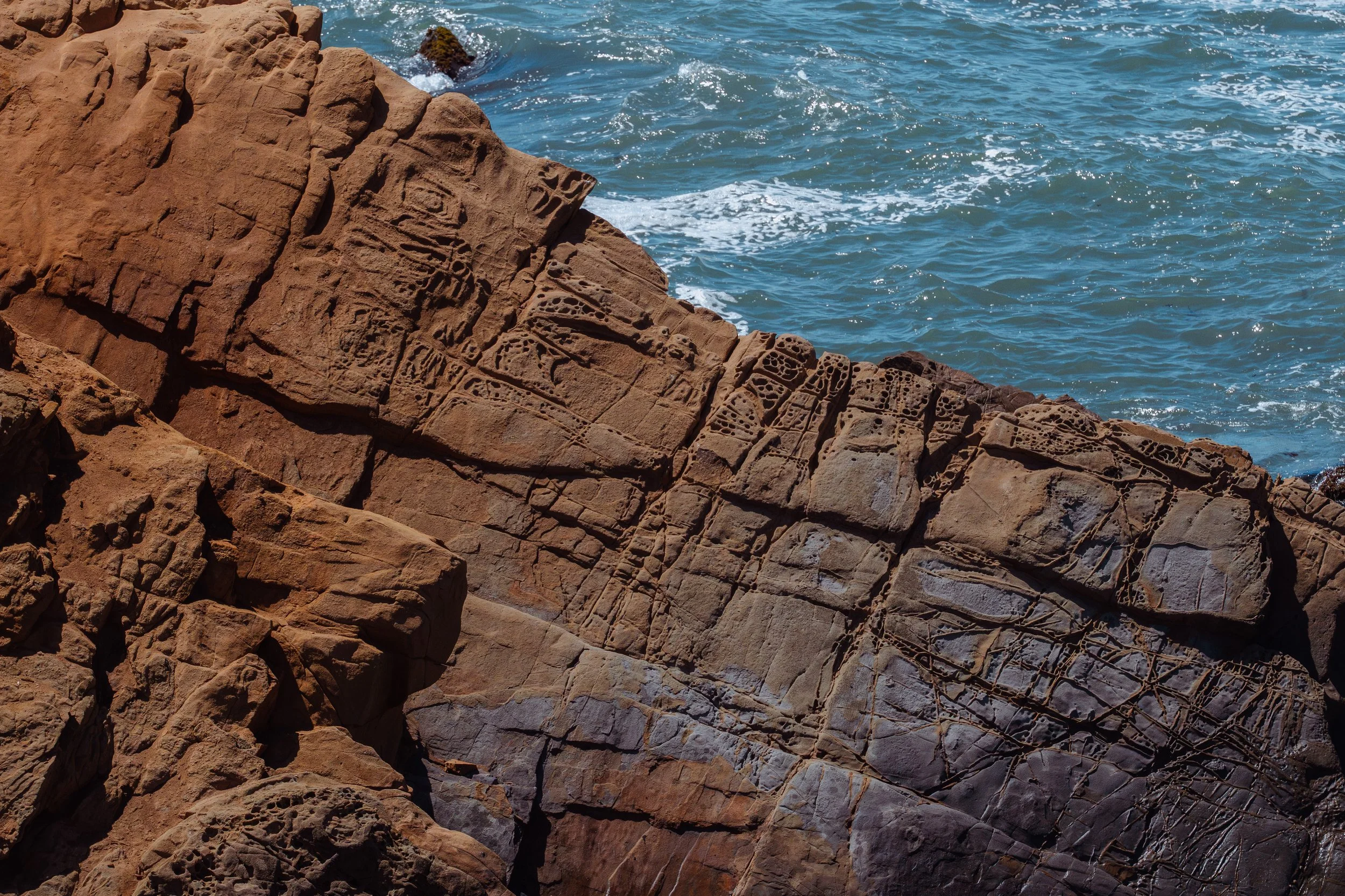 Angular shoreline rock carved by salt and sea beside blue water