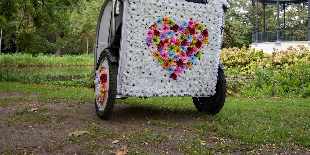 Wedding rickshaw decorated with white flowers and a coloured flower heart, beside the water in an Amsterdam park