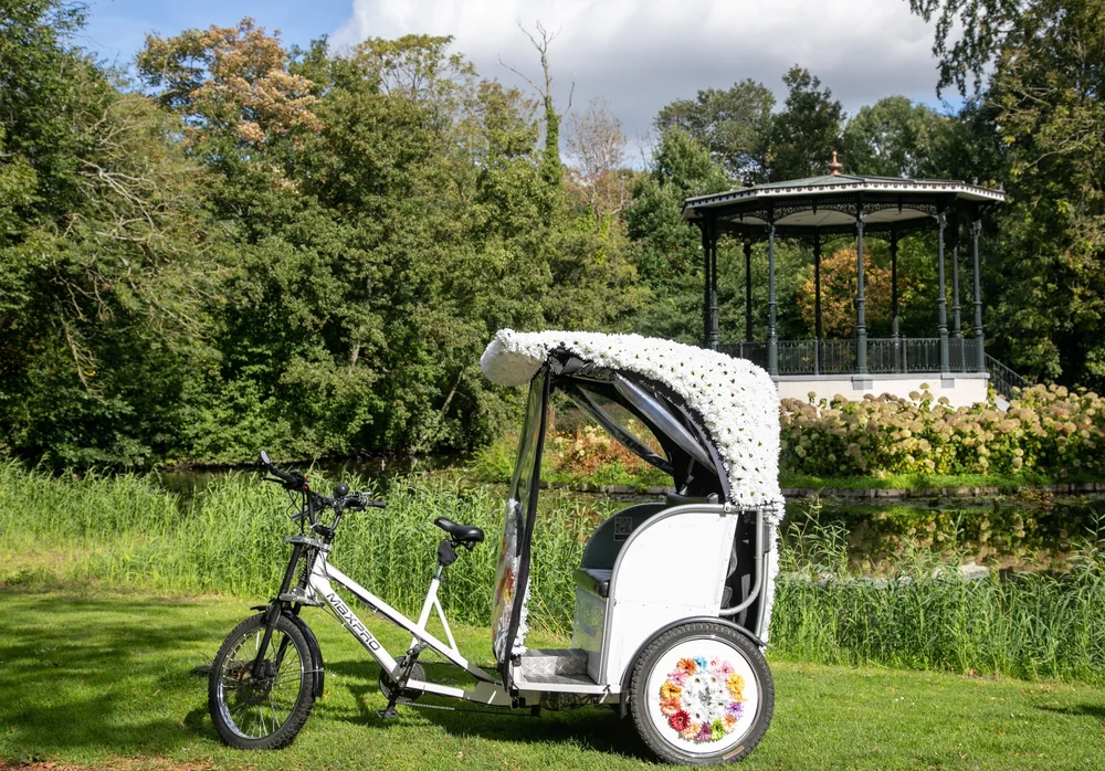 Side view of a white flower-decorated wedding rickshaw with flower-trimmed wheels in an Amsterdam park