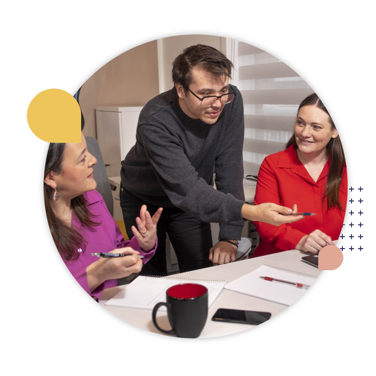 Three Indigenous colleagues share ideas during a workplace discussion with notebooks and pens.