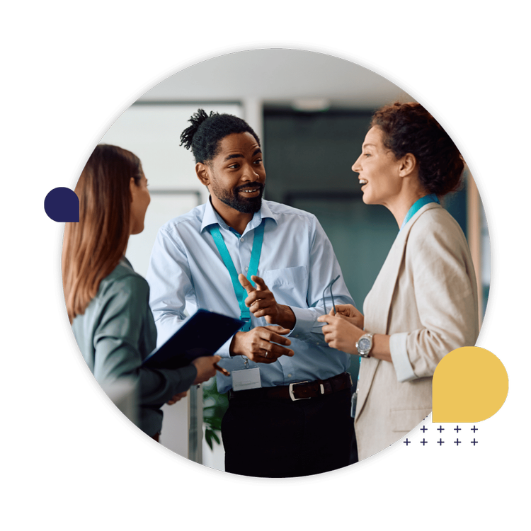 Three professionals wearing conference badges talk together in a modern office