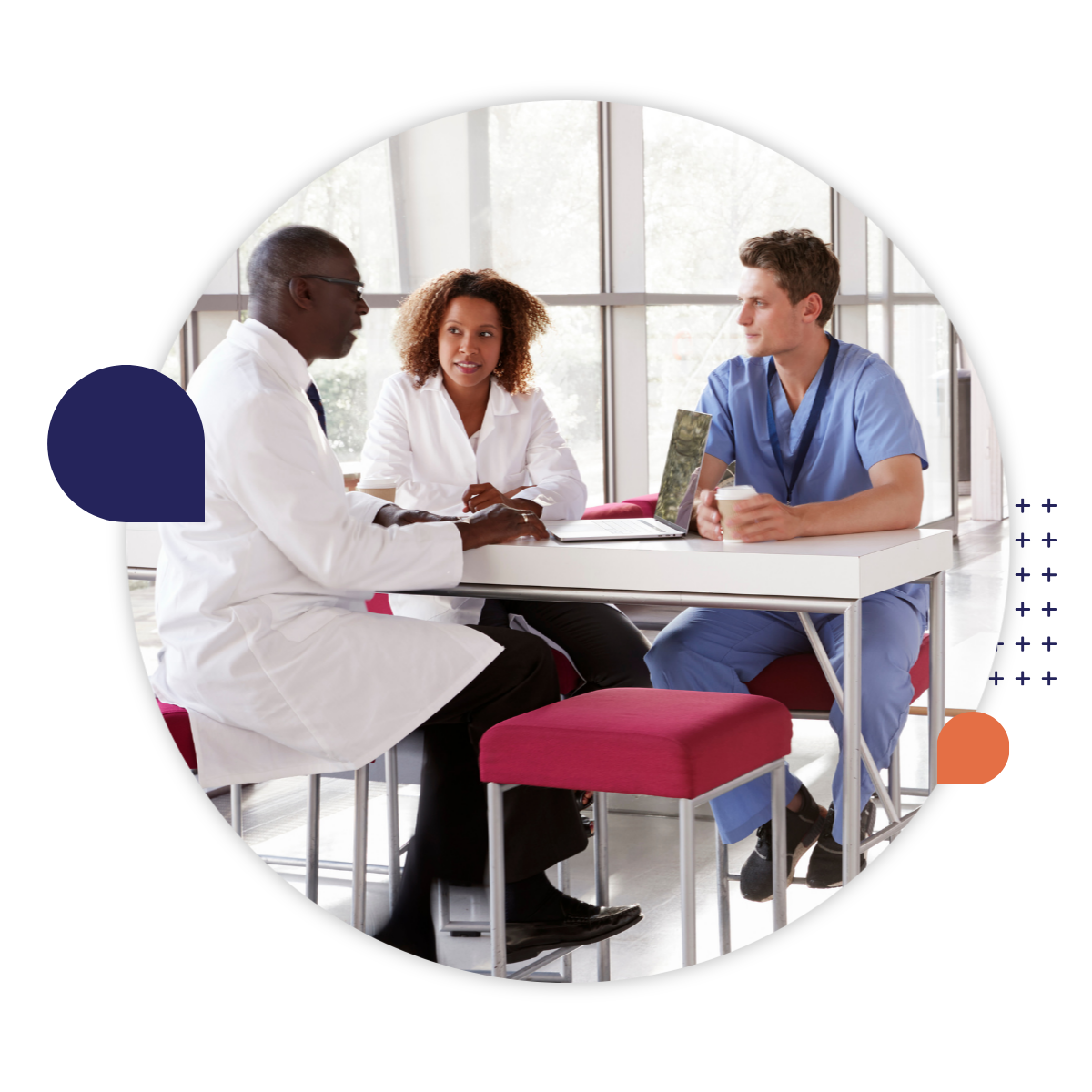 Three healthcare professionals sit around a table in a bright clinical setting, engaged in conversation with a laptop open between them.
