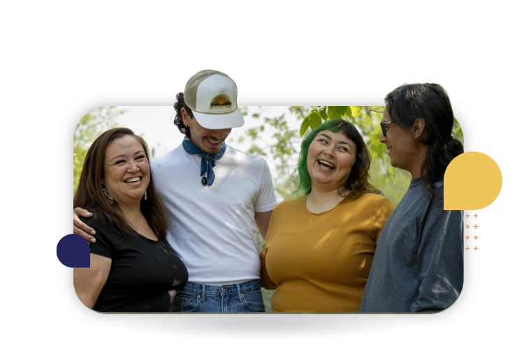 Four Indigenous people stand together outdoors, smiling and sharing a joyful moment.