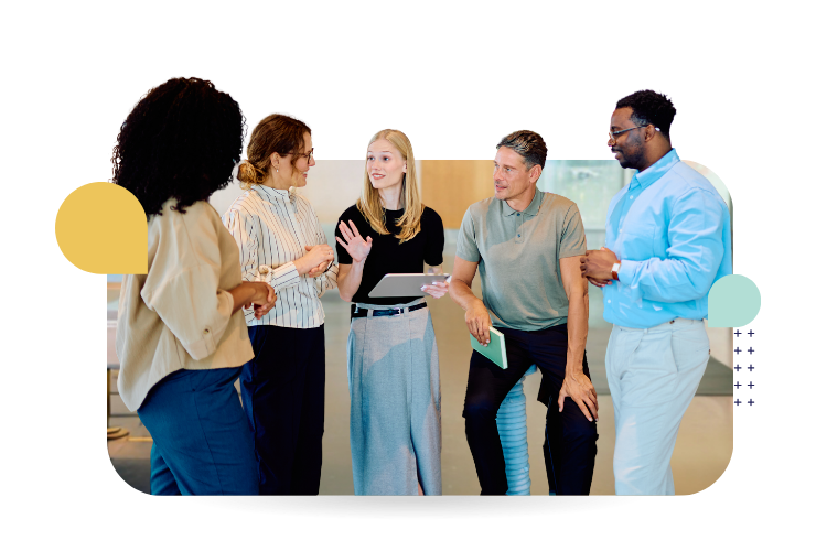 A diverse group of five coworkers stands together in a bright office, engaged in conversation. One woman holds a tablet while others listen and smile.