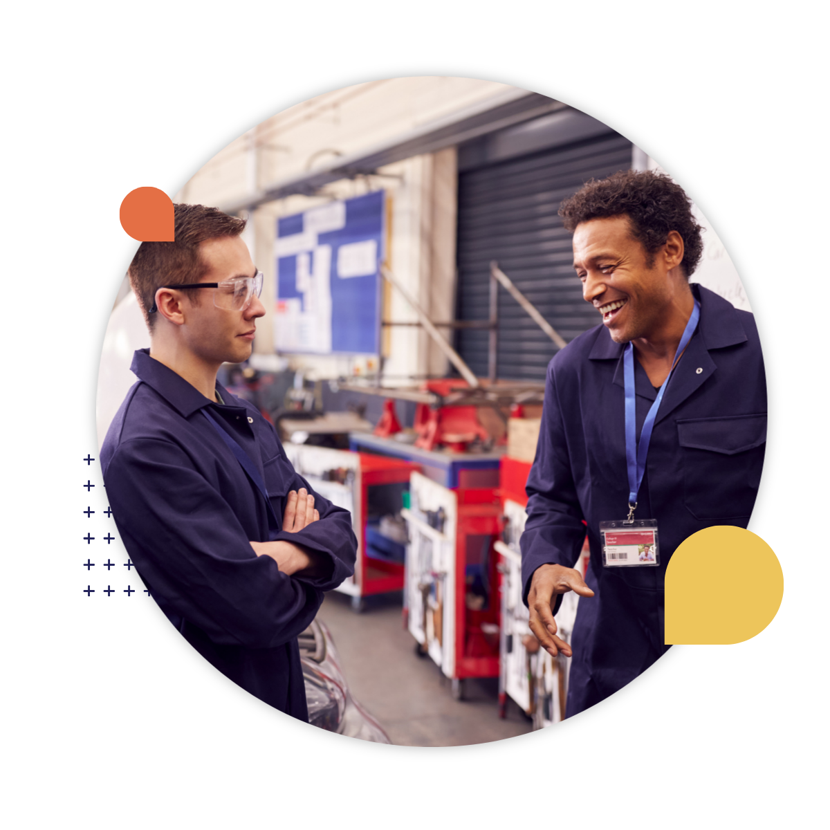 Two coworkers in work uniforms talk and smile together in an industrial workshop.