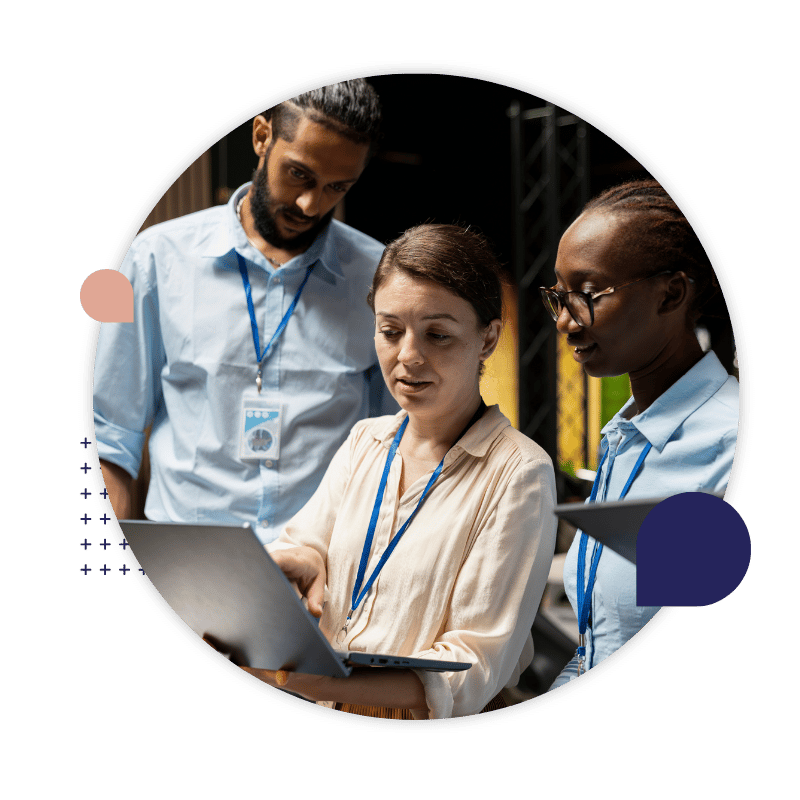 Three colleagues review information together on a laptop in a warehouse.