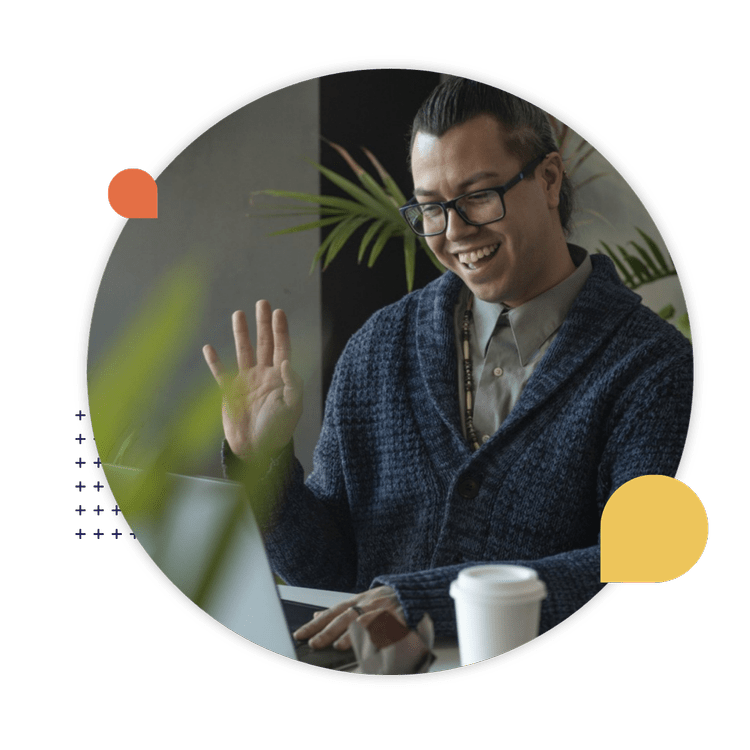 An Indigenous professional smiles and waves during a virtual meeting on a laptop.