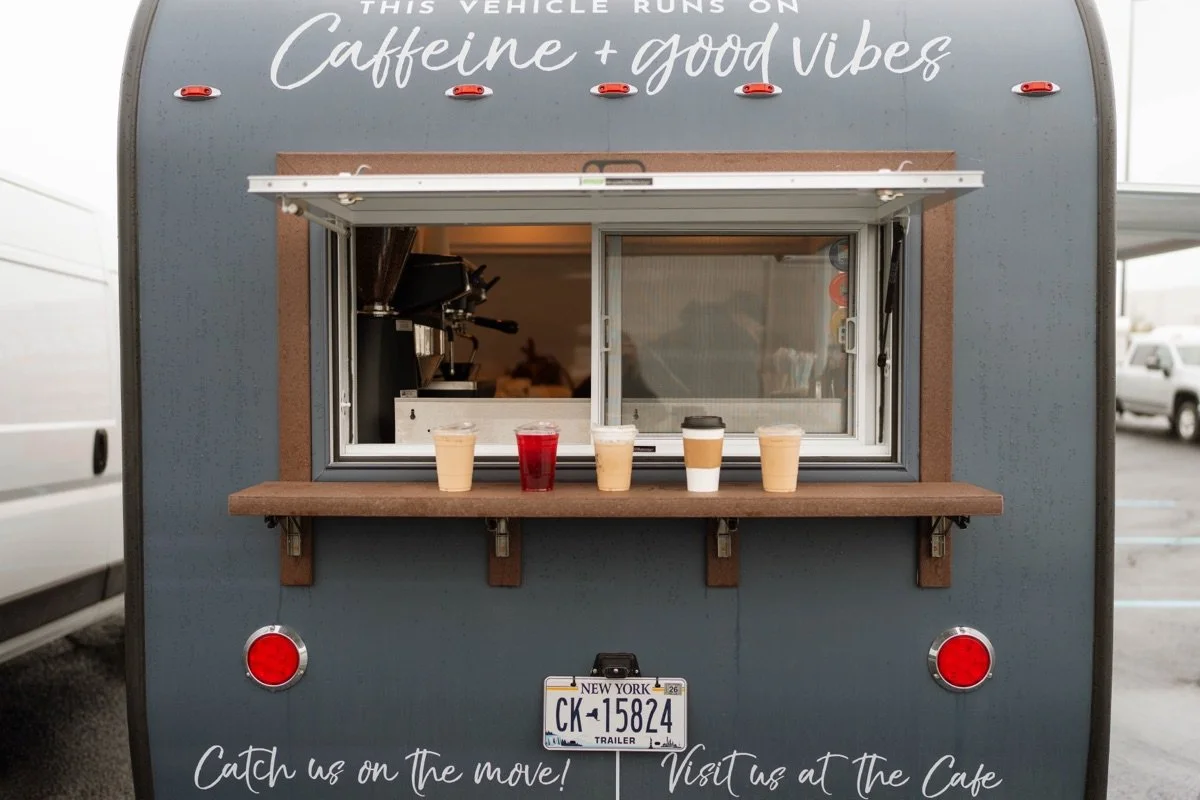 Rear exterior of Blueberries & Lace’s gray Aero Build coffee trailer with an open service window and serving shelf.