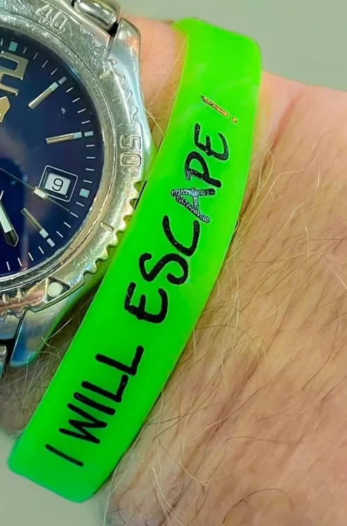 Green silicone wristband reading I Will Escape, worn on a wrist