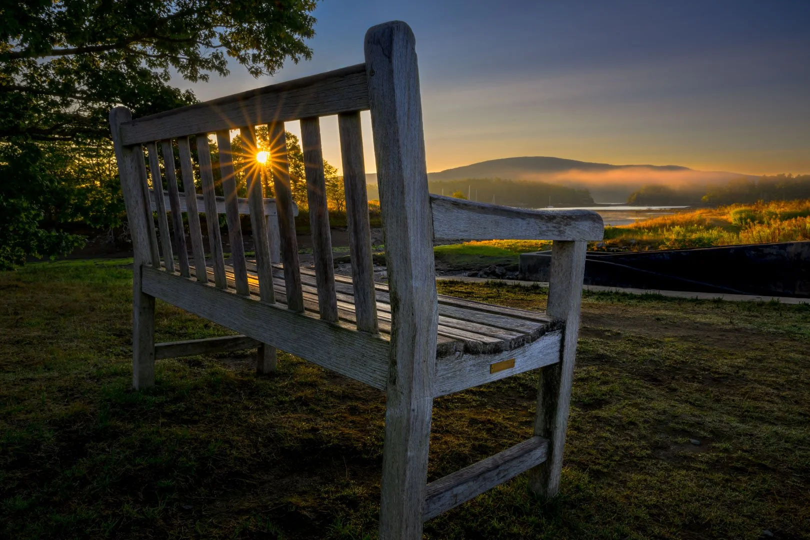 Sunlight shining through a wooden bench beside misty water and distant hills