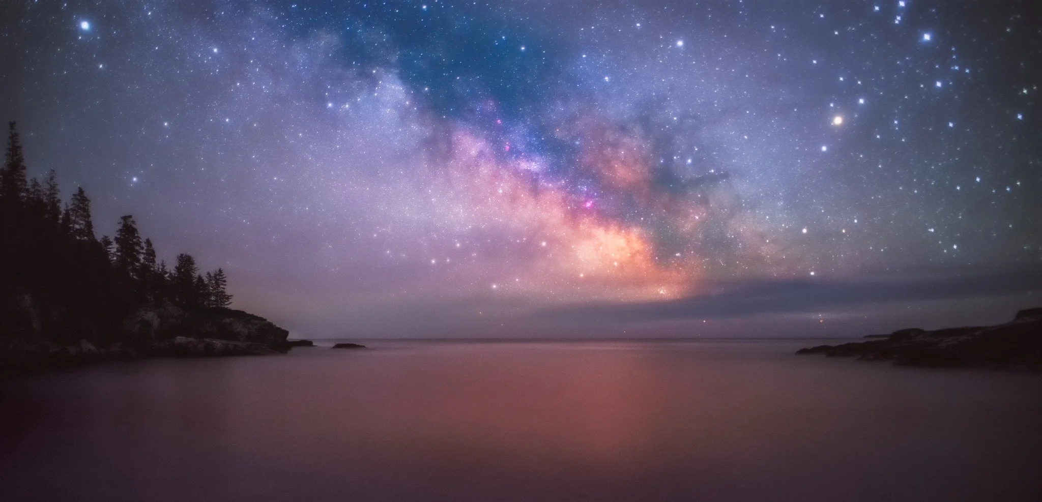 Milky Way over a quiet coastal cove and silhouetted trees