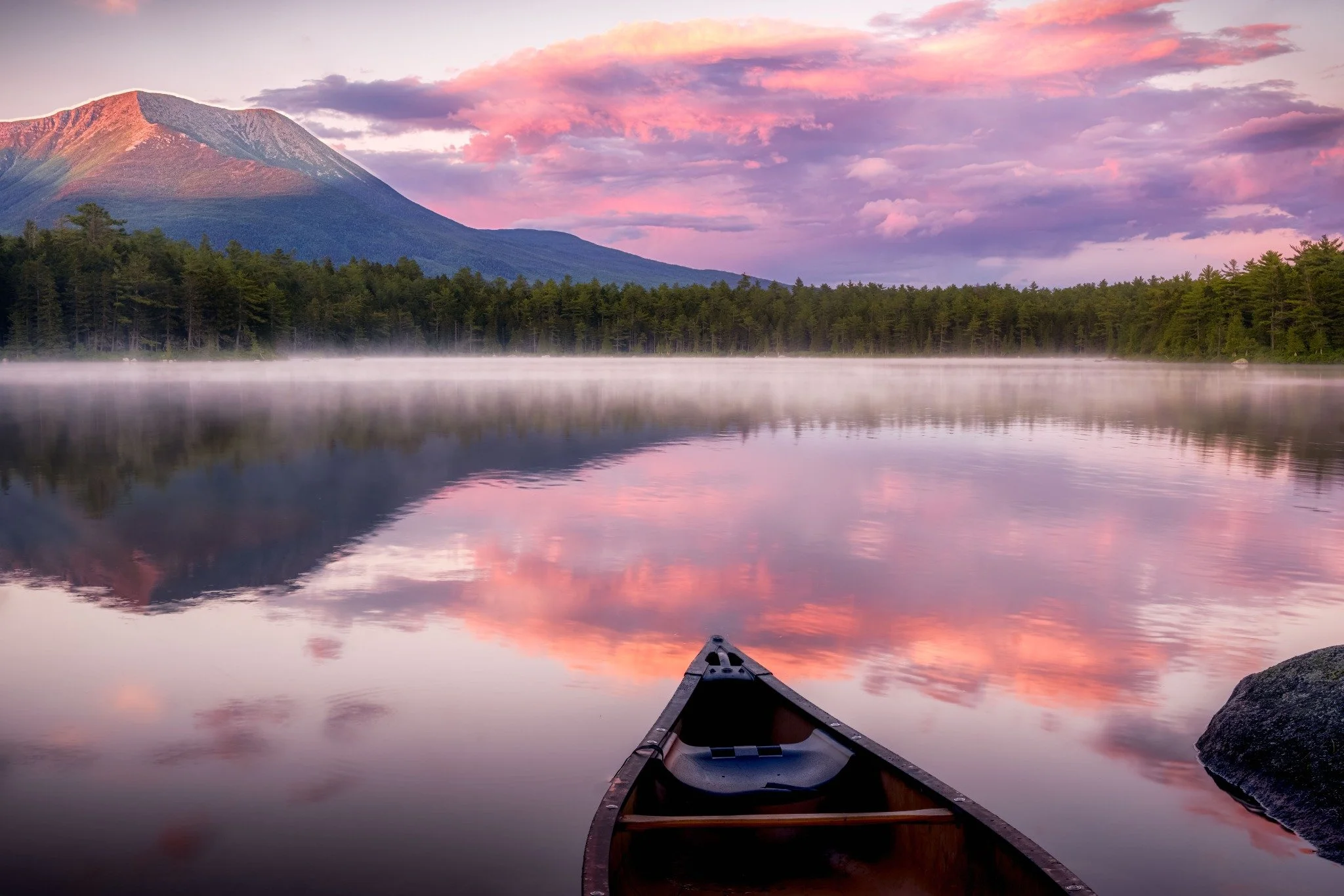 Canoe on a misty pond reflecting a mountain and pink evening clouds