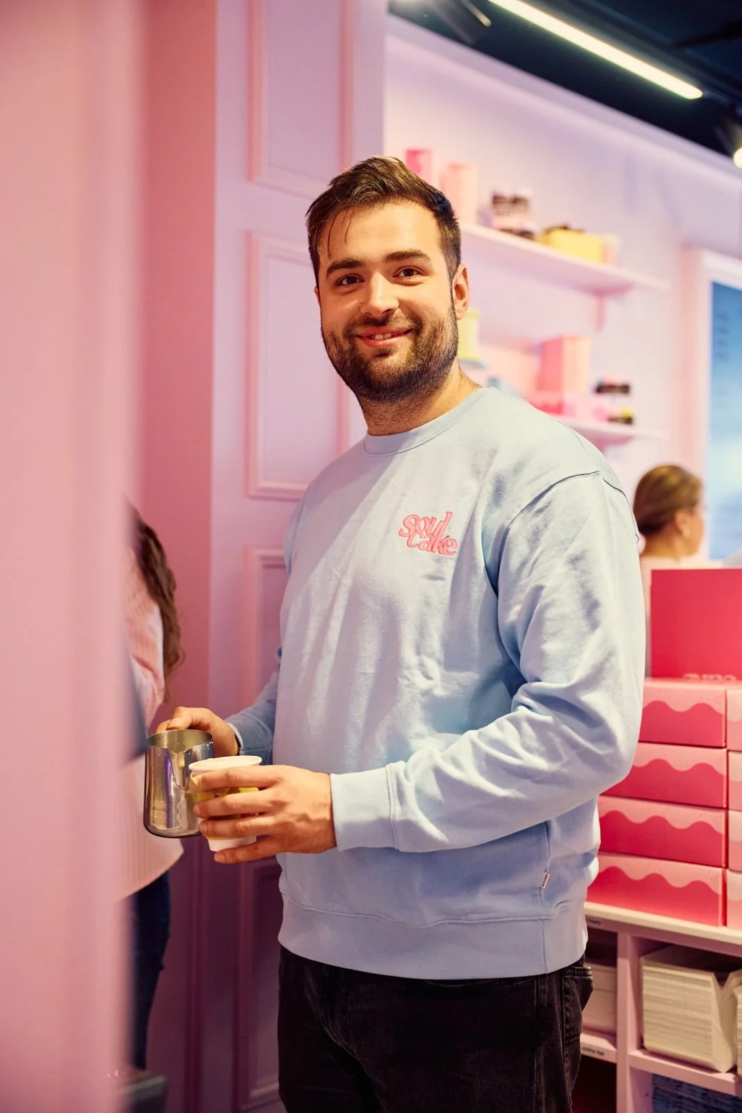 Mann i lyseblå Soulcake-genser med melkemugge og kaffekopp i den rosa kaféen