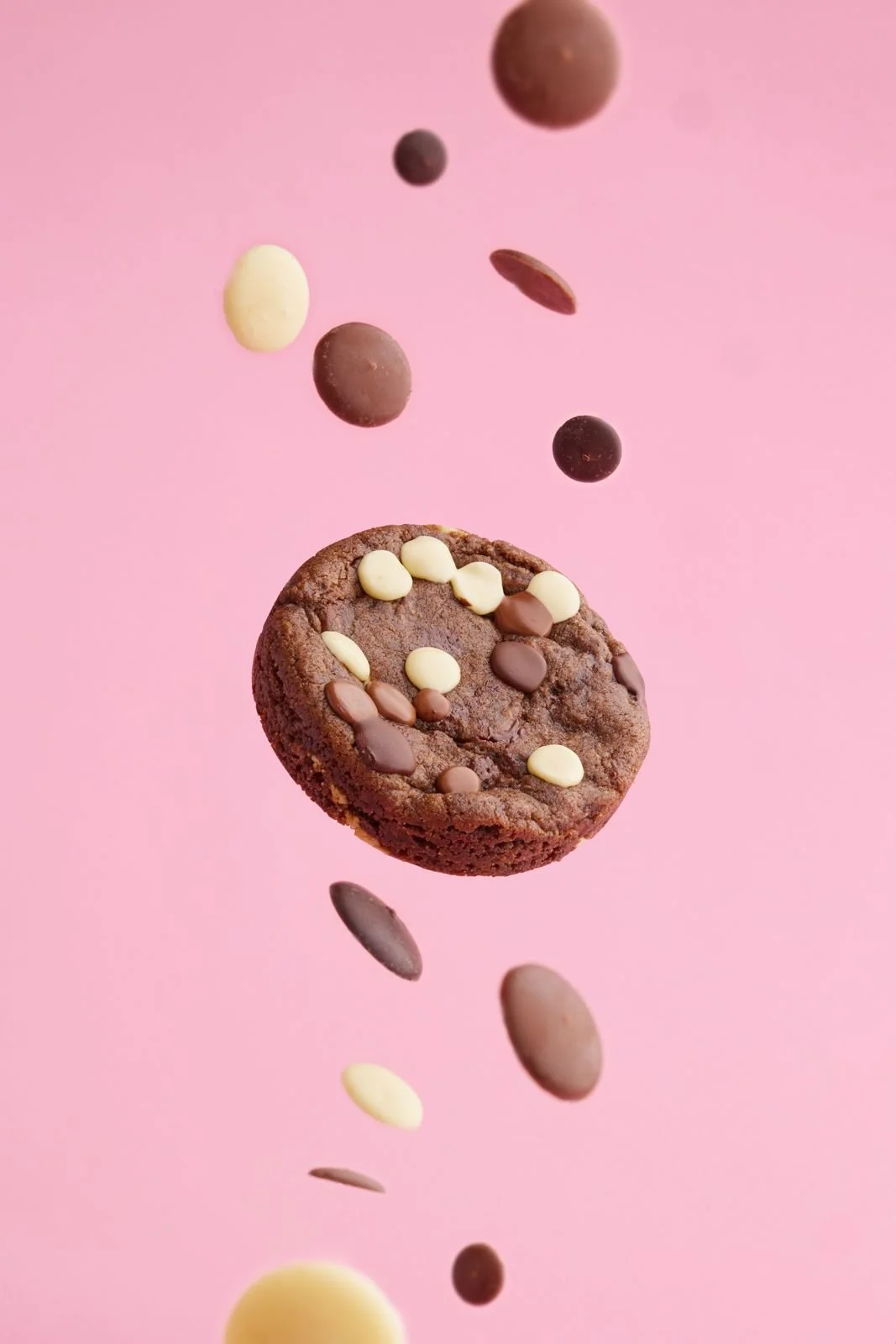 Cookie med hvit og mørk sjokolade svever i luften mot rosa bakgrunn