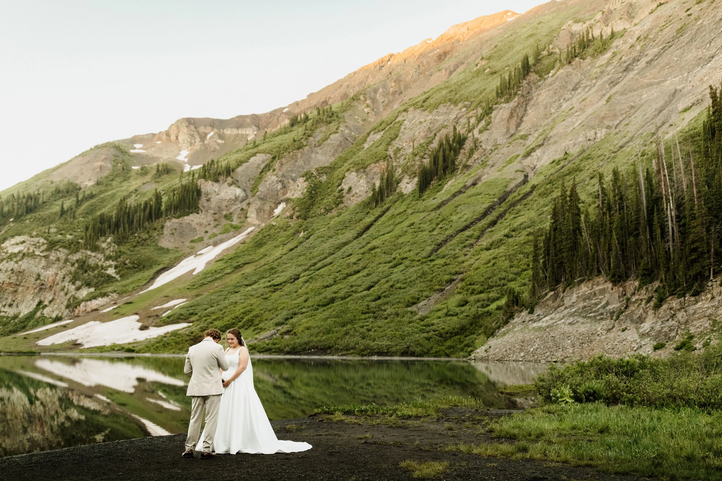 A couple reads vows to each other while sunlight begins on the mountain tops at Emerald Lake outside of Crested Butte, Colorado off of Gothic road
