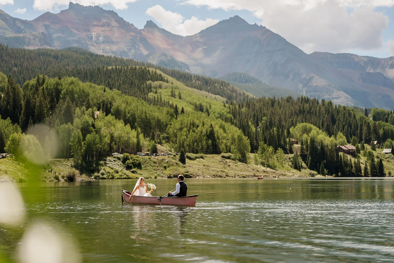 A couple in wedding clothes sit in a red canoe in front of mountains