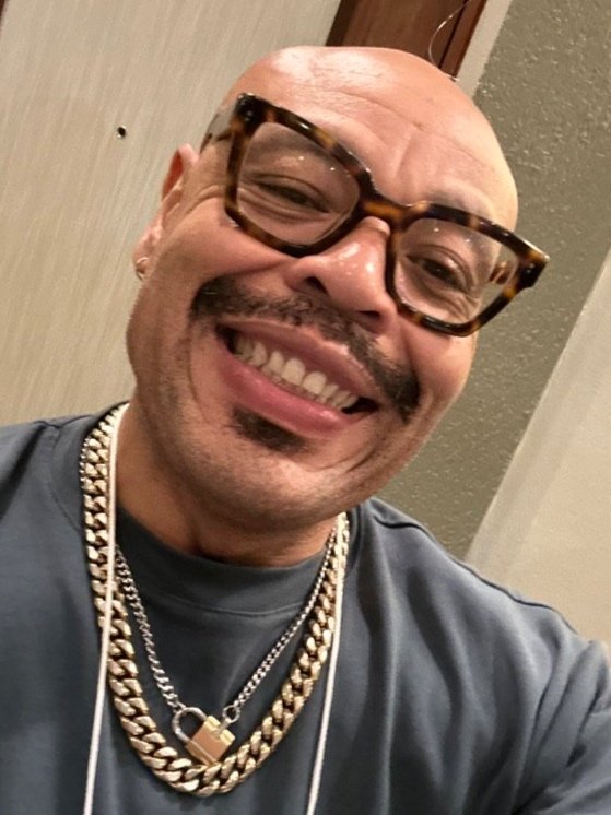 Michael Crumpler, a Black person smiling with brown eyeglasses, wearing an orange-ish brown collared shirt with wooden buttons.