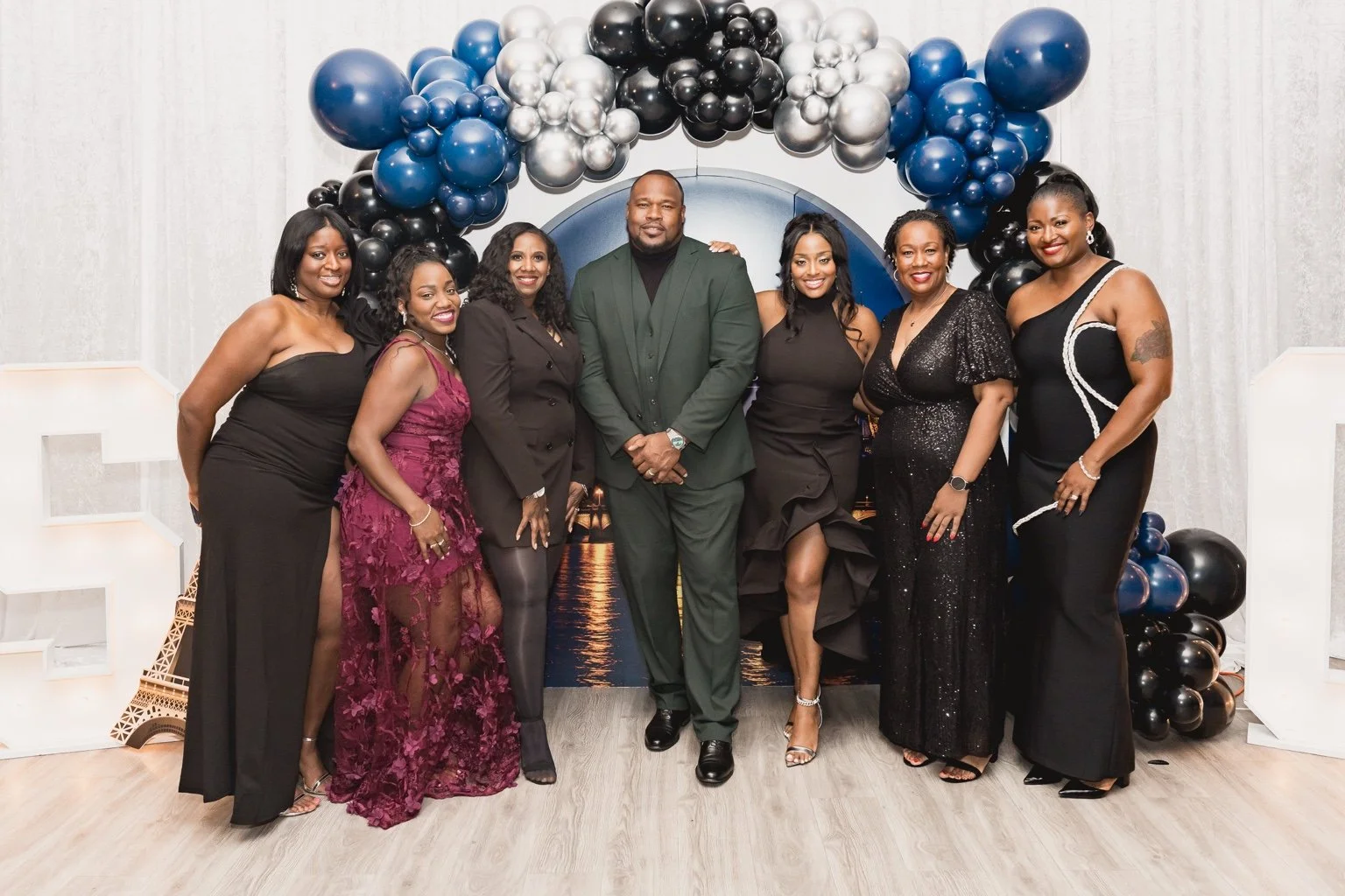 Seven guests pose beneath blue, silver and black balloons at the reunion.