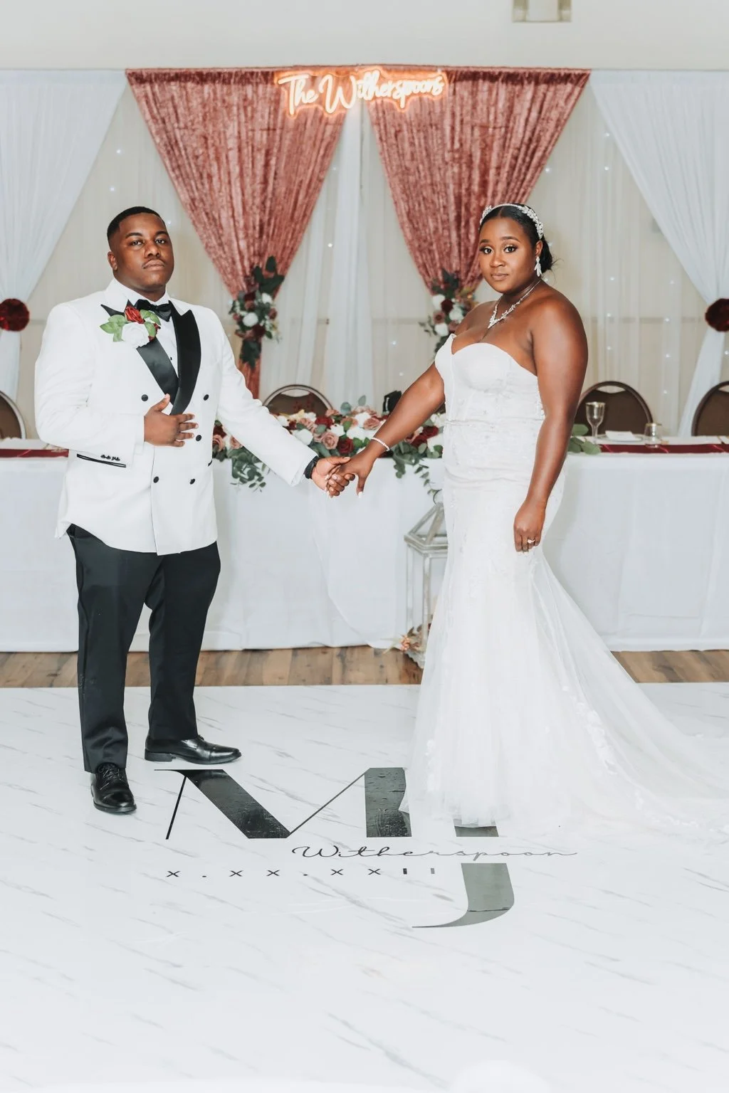 Bride in a white gown and groom in a white dinner jacket holding hands for a formal wedding portrait.