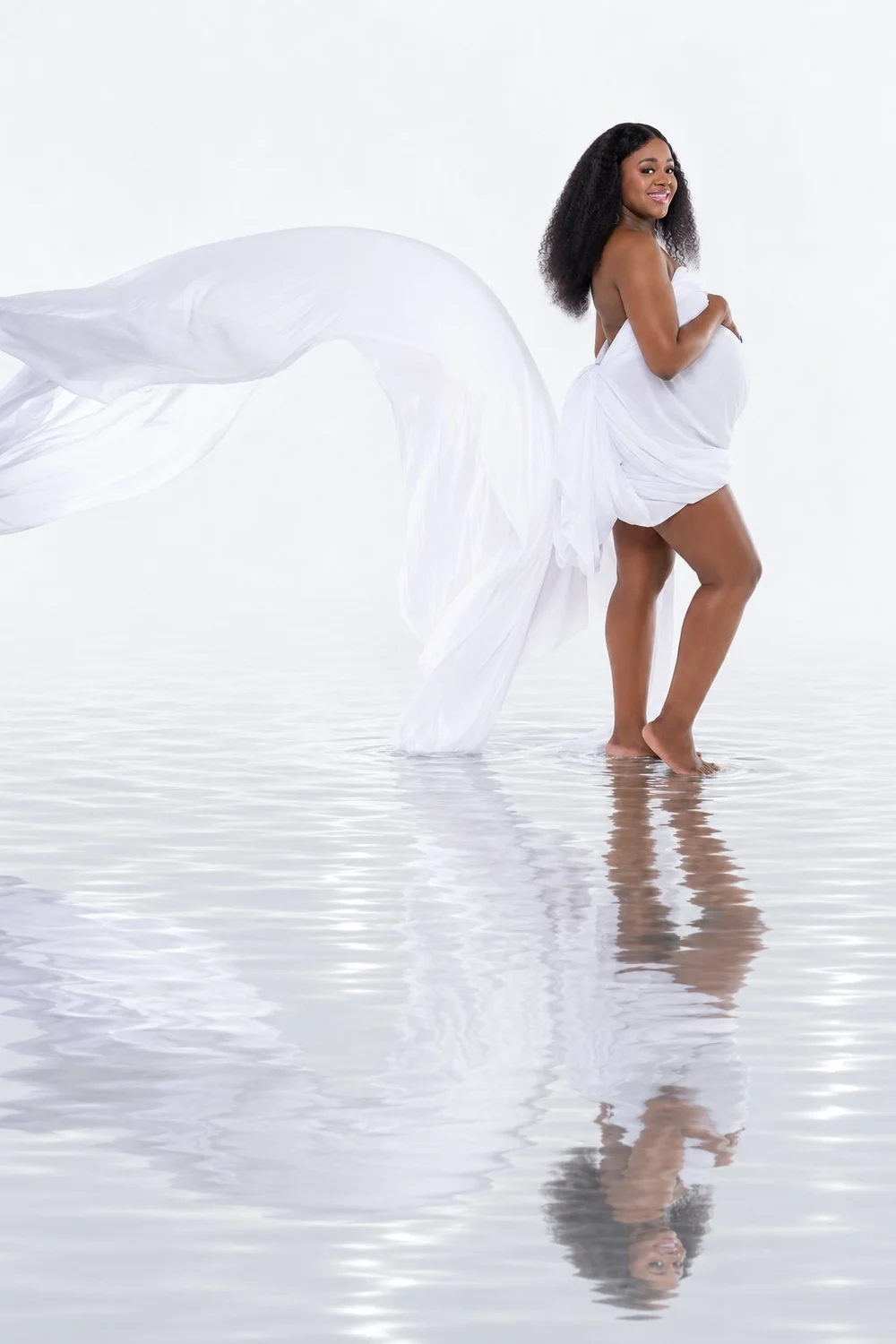 Capria smiling in flowing white fabric above a rippled water reflection