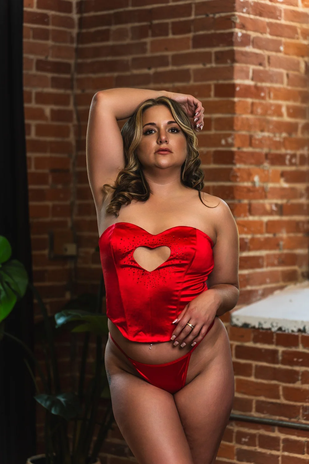 Alicia in red beside a brick wall with one arm raised