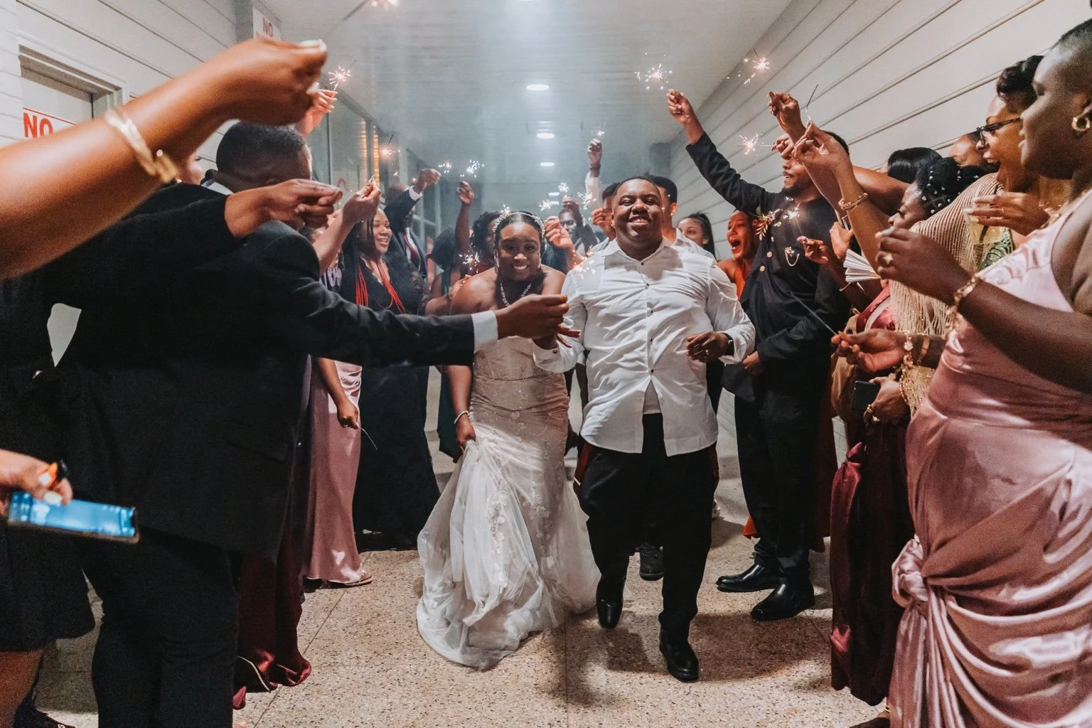 Smiling newlyweds walking between rows of guests holding sparklers during their wedding exit.