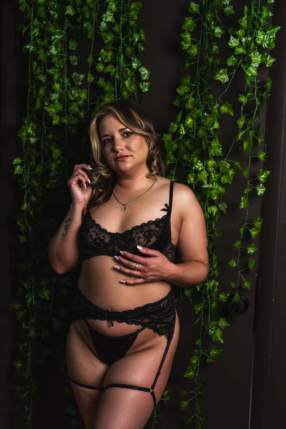 Alicia in black lace standing against a backdrop of green foliage