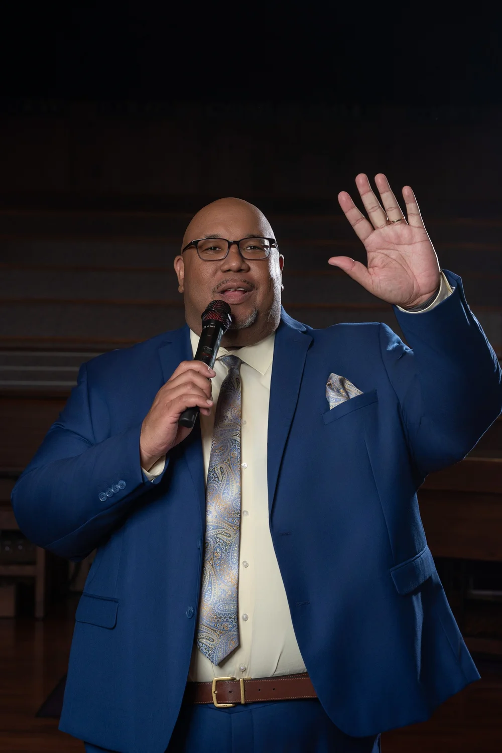 Dr. Michael Dorsey in a blue suit holding a microphone with one hand raised