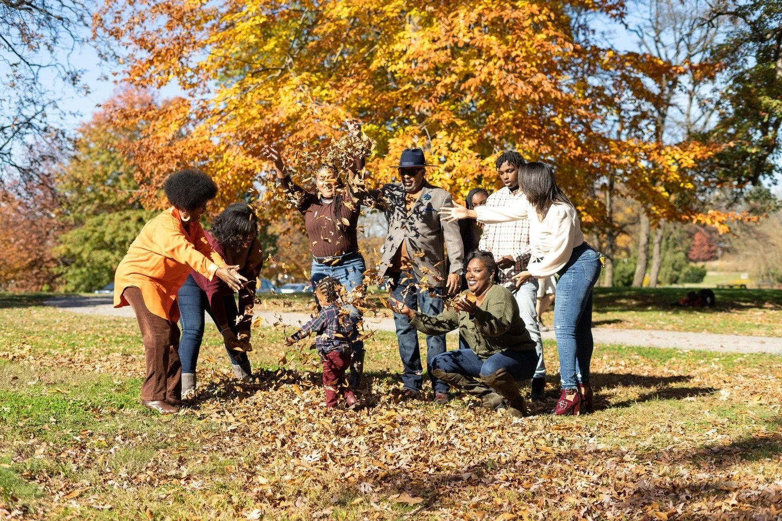 The Wiggins family laughing and tossing autumn leaves together in a park