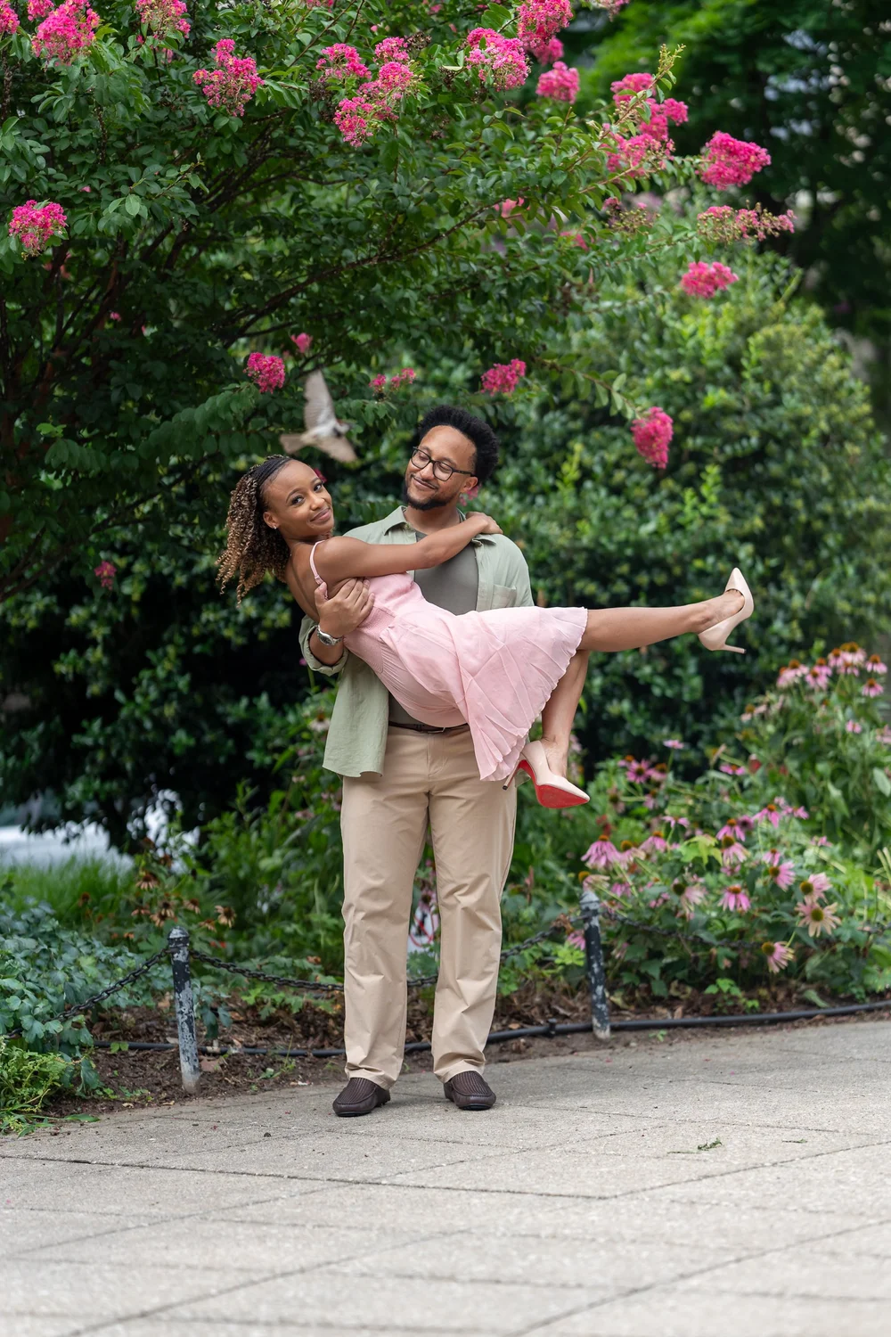 A playful lift beneath pink flowers during Brook and Morgan’s engagement session