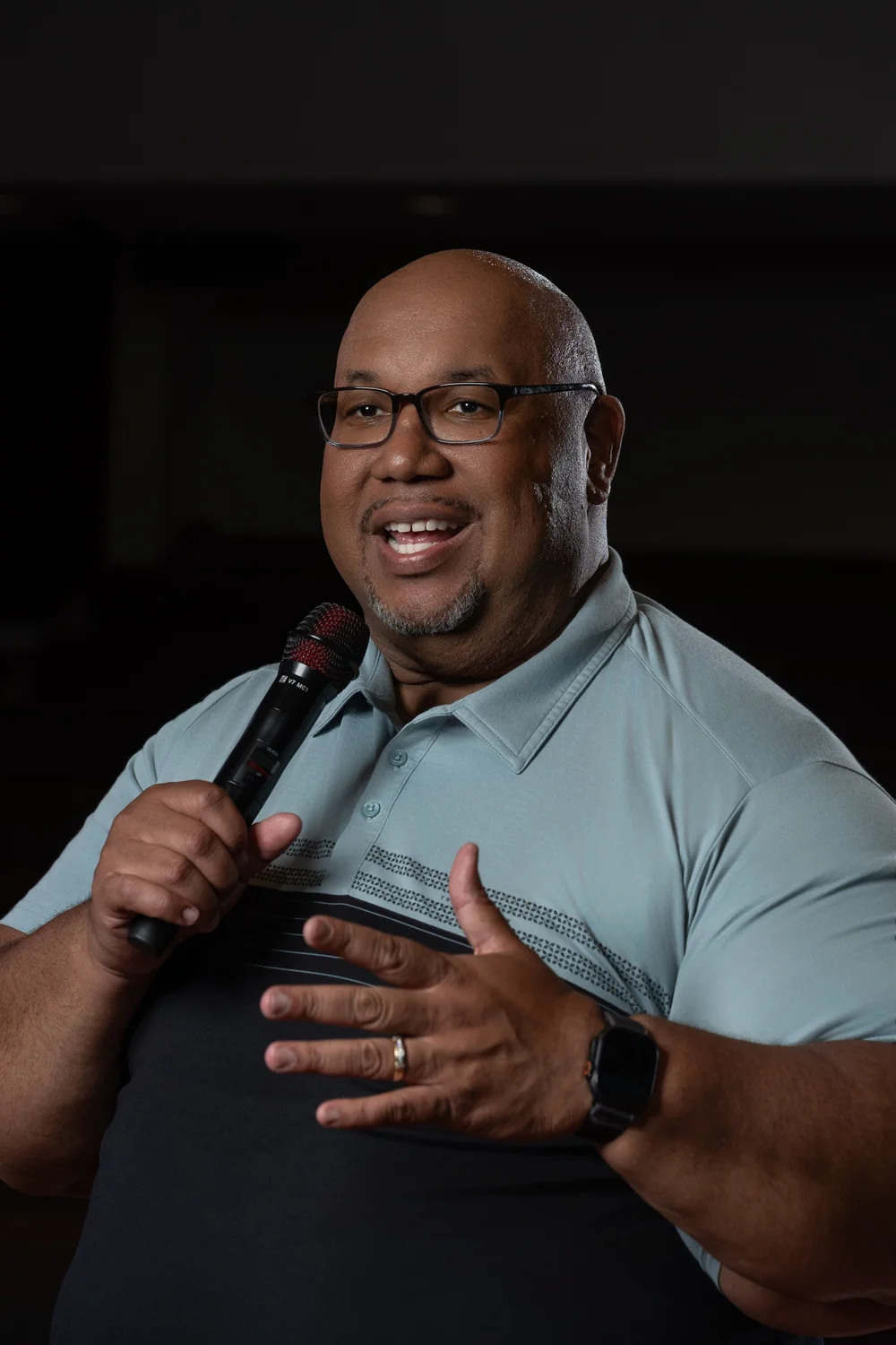 Dr. Michael Dorsey smiling and gesturing with an open hand while holding a microphone