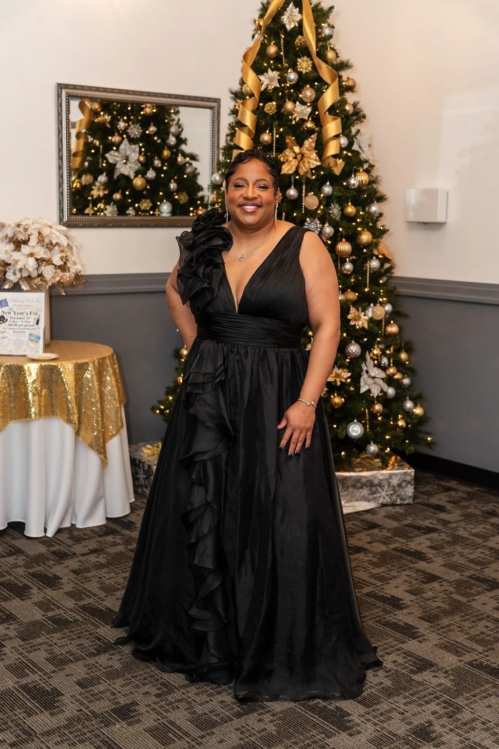 Angelia posing in a black gown beside a gold-decorated Christmas tree
