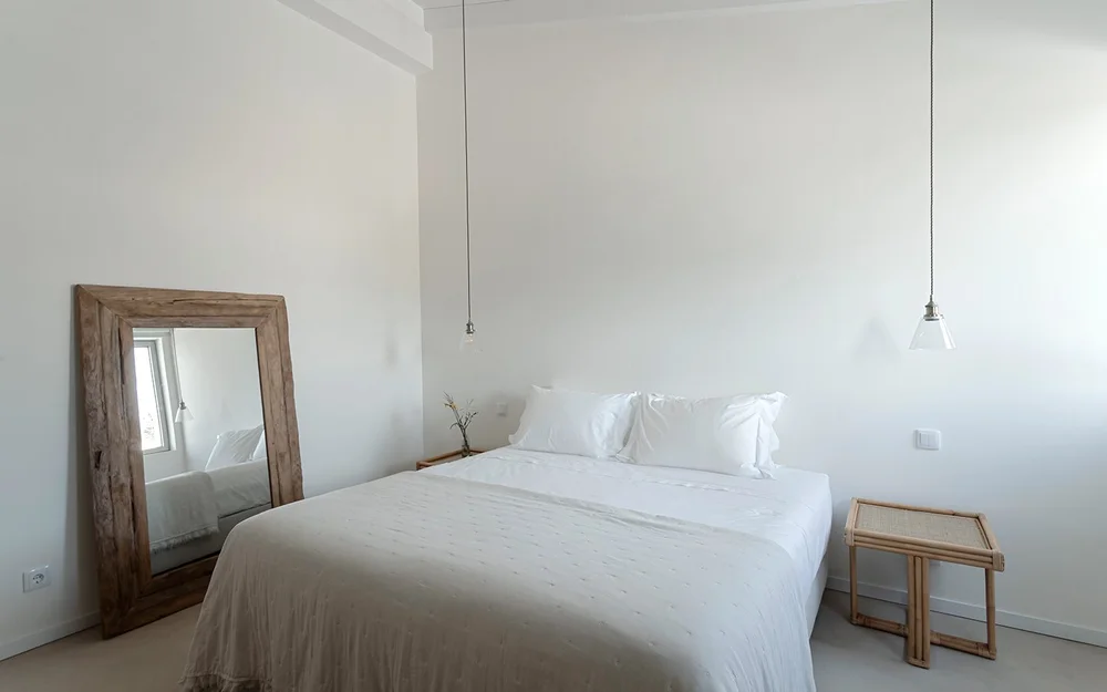 Apartment bedroom with white bedding and a timber-framed mirror at Amaria